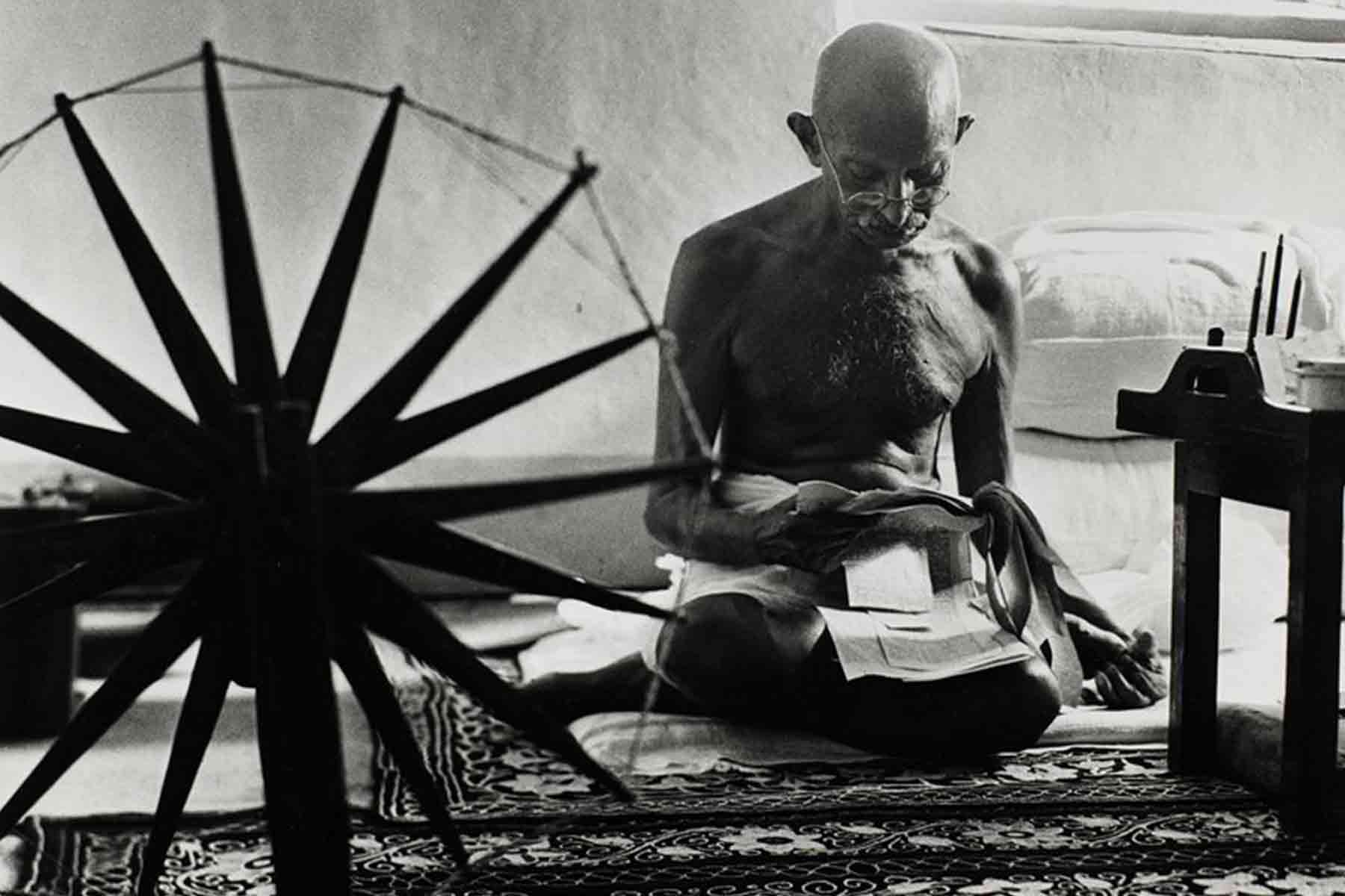 Mahatma Gandhi reading next to his spinning wheel (© Estate of Margaret Bourke-White)