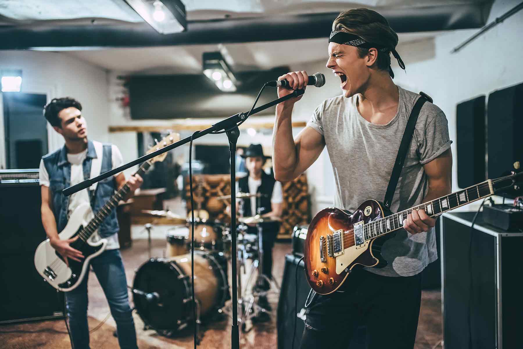 A young rock band rehearsing in a studio with a lead singer, guitarist, and drummer. A young rock band rehearsing in a studio with a lead singer, guitarist, and drummer.